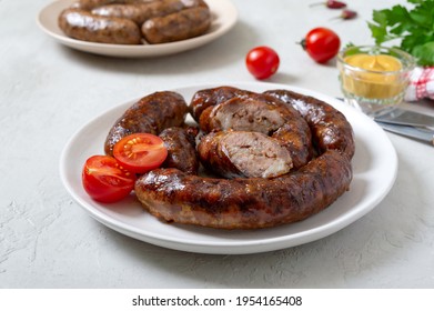 Juicy homemade baked sausage on a plate with mustard and fresh tomatoes.