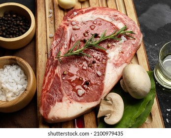 Juicy Raw Steak With Olive Oil And Special Seasoning On A Wooden Board With Grilled Mushrooms. Top View, Close-up