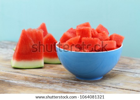 Juicy and refreshing cubes of watermelon in blue bowl on wooden surface
