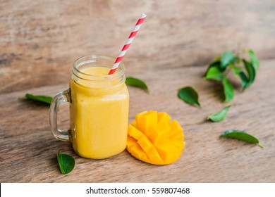 Juicy smoothie from mango in glass mason jar with striped red straw on old wooden background. Healthy life concept, copy space.