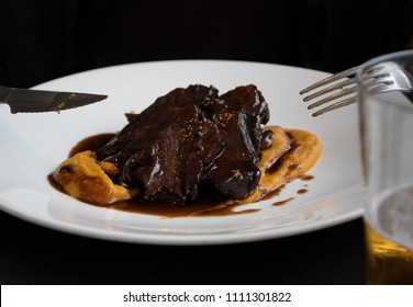 Juicy Stewed Beef In Sauce Served With Sweet Potato Puree. Fork And Knife Already With Sauce Stains. Glass Of Beer.