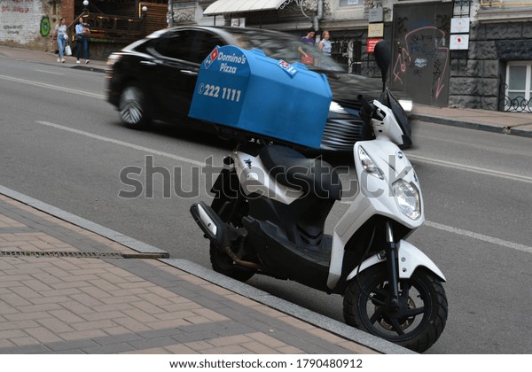 July 2020\
in Kyiv, Ukraine. A photo of a Domino pizza delivery\
motorbike/moped scooter parked in the street.\
