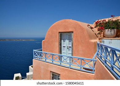 July 31, 2019. Traditional Adobe House Facade With Coral Painted Arched Wall, Light Blue Wooden Door And Stone Steps In Oia, Santorini Island Cyclades, Greece. 