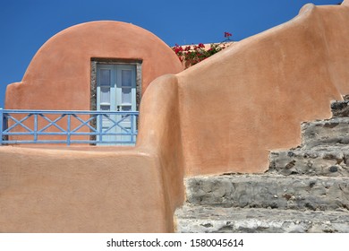 July 31, 2019. Traditional Adobe House Facade With Coral Painted Arched Wall, Light Blue Wooden Door And Stone Steps In Oia, Santorini Island Cyclades, Greece. 