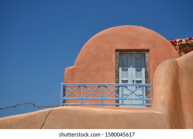 July 31, 2019. Traditional Adobe House Facade With Coral Painted Arched Wall, Light Blue Wooden Door And Stone Steps In Oia, Santorini Island Cyclades, Greece. 