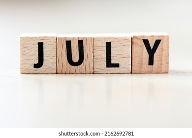 JULY word arranged with wooden letters on a light background.
