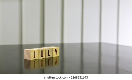 JULY Word On Wooden Cube On Black Gloss Wooden Table. Selected Focus