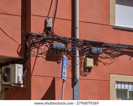 A jumble of electrical wires and boxes is attached to a red building.