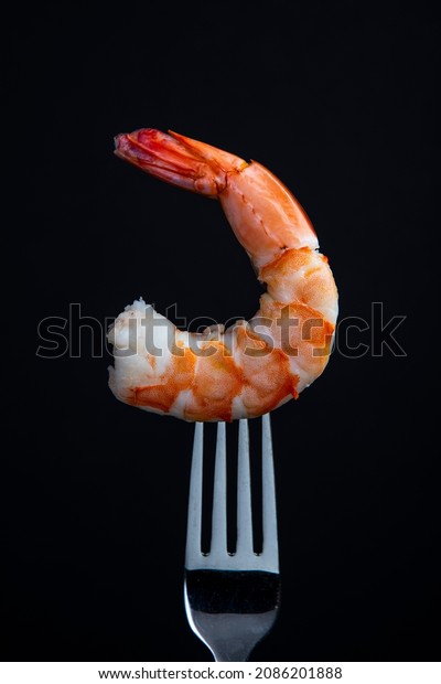 Jumbo Cooked shrimp on a fork isolated on\
black background.