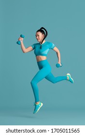 In Jump. Beautiful Young Female Athlete Practicing In Studio, Monochrome Blue Portrait. Sportive Fit Brunette Model With Weights. Body Building, Healthy Lifestyle, Beauty And Action Concept.