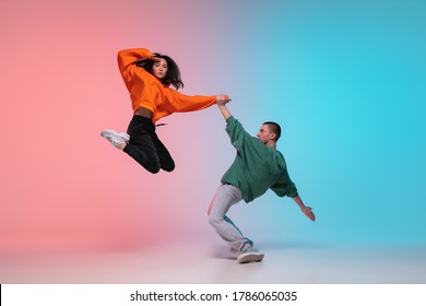 Salto. Niño y niña bailando hip-hop con ropa elegante en un fondo de gradiente colorido en la sala de baile de neón. Cultura juvenil, movimiento, estilo y moda, acción. Retrato de moda. Danza callejera.