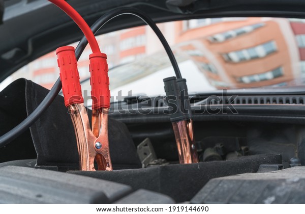 Jump cables on car low power\
battery. Black and red. Broken car start attempt. Selective\
focus.