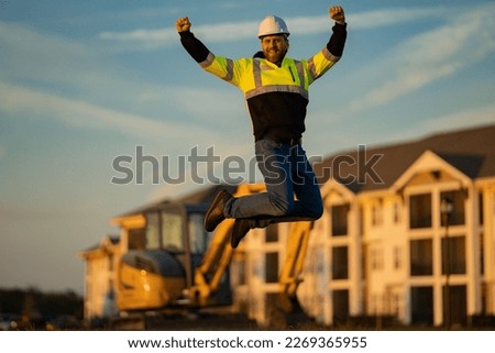 Jump excited worker. Builder, construction worker in helmet at construction site. Industry engineer worker in hardhat near bulldozer or digger tractor. Concept of construction industry.