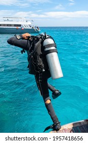 Jump Of An Instructor In Scuba Diving Equipment From A Boat To Dive Into The Waters Of The Red Sea, One Leg Froze In The Air, The Other Comes Off The Side Of The Boat,a Moored Vessel In The Background