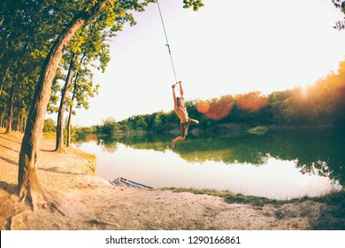 Jump Into The Water. A Man Is Resting On The Lake. A Swing From A Rope And A Stick. Active Recreation In Nature. Summer Fun. A Man Is Riding A Swing. Fisheye Lens.
