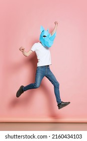 Jumping. Creative Portrait Of Young Man In White T-shirt With Cardboard Animal Mask On His Head Isolated On Pink Background. Concept Of Art, Fashion, Theater, Funny Meme Emotions. Copy Space For Ad