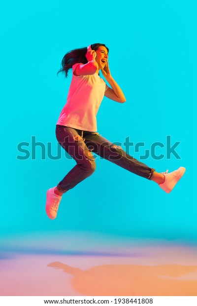 Jumping, dancing. Full-length portrait of young\
beautiful girl, fashion model isolated on blue background in neon\
light. Concept of human emotion, youth culture, online education.\
Copy space for ad