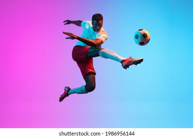 Jumping, flying. One young African man, professional soccer football player training isolated on gradient blue pink background in neon light. Concept of action, energy, sport. Copy space for ad - Shutterstock ID 1986956144
