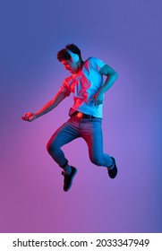 Jumping, Flying. Stylish Young Asian Man Isolated Over Lilac Color Studio Background In Pink Neon Light. Concept Of Human Emotions, Facial Expression, Youth Culture, Diversity. Listening To Music