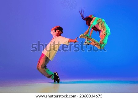 Jumping, flying. Two young people, guy and girl, dancing contemporary dance, hip-hop over blue background in neon light. Modern dance aesthetics concept. Copyspace for ad