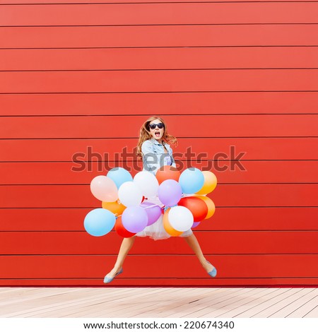 Jumping girl with colorful balloons in her hand. Outside. Red background. Outside