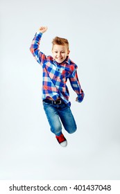 Jumping little boy in the colorful plaid shirt, blue jeans, gumshoes. Isolated.