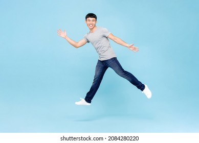 Jumping Shot Of Ecstatic Young Asian Man With Open Arms Isolated In Blue Studio Background