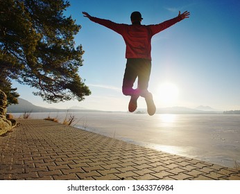 Jumping Silhouette Against Low Sun. Workout At The Lake Beach. Winter Morning Excercise, Ice Cover Lake And Create Nice Reflection