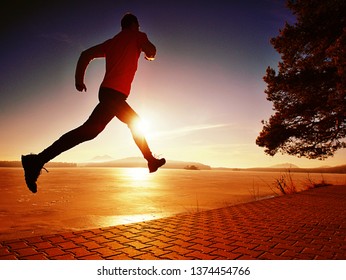 Jumping Silhouette Against Low Sun. Workout At The Lake Beach. Winter Morning Excercise, Ice Cover Lake And Create Nice Reflection