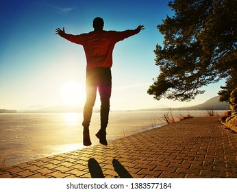 Jumping Silhouette Against Low Sun. Workout At The Lake Beach. Winter Morning Excercise, Ice Cover Lake And Create Nice Reflection