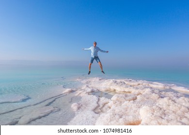 Jumping Tourist On Shore Of The Dead Sea. Jordan Landscape