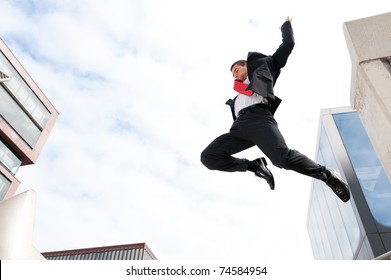 Jumping young buiness man in front of buildings