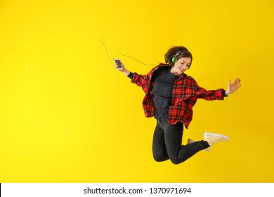 Jumping young woman with with headphones and mobile phone against color background