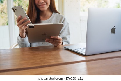 Jun 16th 2020 : An Asian Woman Holding And Using Iphone 11 Pro Max Smart Phone And Apple New Ipad Pro 2020 Tablet Pc With Apple MacBook Pro Laptop Computer On Wooden Table , Chiang Mai Thailand