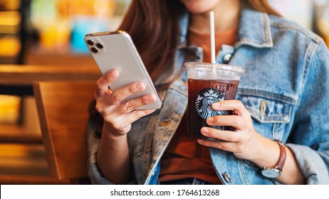 Jun 16th 2020 : A woman holding and using Iphone 11 Pro Max smart phone while drinking iced coffee at Starbucks coffee shop , Chiang mai Thailand