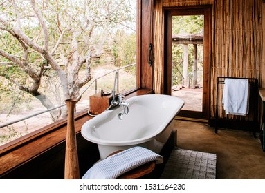 JUN 20, 2011 Serengeti, Tanzania - Villa Resort Bathroom Luxury White Bathtub With Forest View Through Bay Window - African Boho Style Safari Camp Lodge Interior Decoration With Wooden Bamboo Wall.