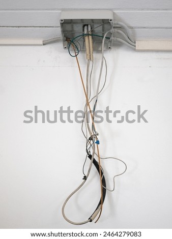 junction box of an open electrical system with dangling wires, white wall background
