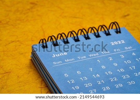 June 2022 - blue spiral desktop calendar against bright orange handmade paper, time and business concept