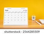 June 2025, Monthly desk calendar for 2025 year on wooden table with alarm clock.