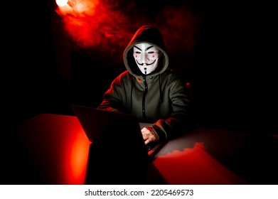 June 5, 2022 Novosibirsk, Russia: Anonymous In A Hood Is Typing On A Laptop In The Dark In Red Smoke. 