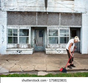 June 8, 2020, Cairo, IL. USA - Old Woman Sweeping Sidewalk In Front Of A Closed Small Family Business On Main Street USA America, Down Economy, Businesses Closing, Shuttered Businesses, American Flag