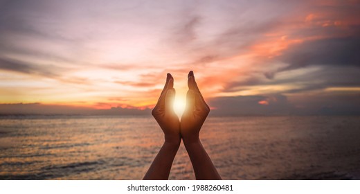 June summer sun solstice concept with silhouette of young woman's hands relaxing, happy meditating and holding sunset against warm golden hour sky on the beach with natural ocean or sea background