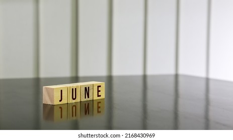 JUNE Word On Wooden Cube On Black Gloss Wooden Table. Selected Focus