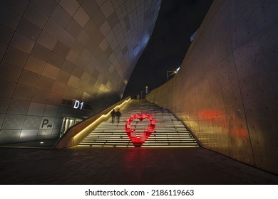 Jung-gu, Seoul, South Korea - December 20, 2021: Long Exposure And Night View Of A Couple Walking Up On Stairs With Heart Shape Culpture Of Red LED Light At DDP
