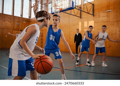 A junior basketball player is dribbling a ball while his rival is trying to steal it on training. Young athletes playing basketball on training at indoor court. A junior basketball team playing basket - Powered by Shutterstock