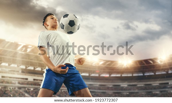 Junior football or soccer player at stadium\
in flashlight. Young male sportive model training. Moment of\
attacking, catching. Concept of sport, competition, winning,\
action, motion,\
overcoming.