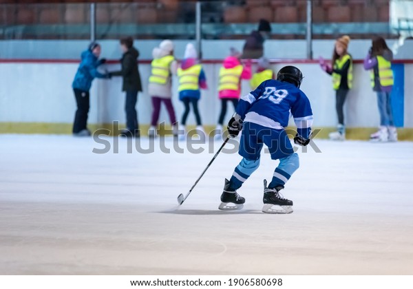 Junior ice hockey player\
demonstrates his skating skills in front of skating school\
students