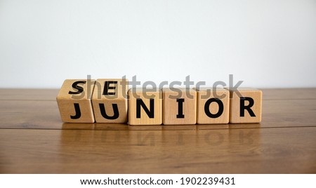 From junior to senior symbol. Turned cubes and changed the word 'junior' to 'senior'. Beautiful wooden table, white background, copy space. Business and junior or senior concept.