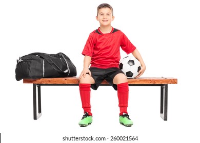 Junior Soccer Player Sitting On A Bench And Holding A Football Isolated On White Background