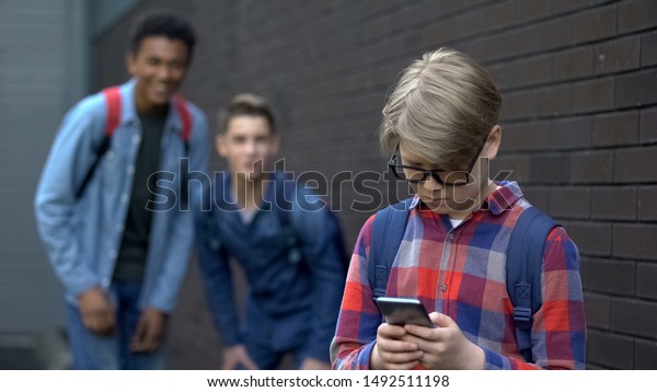 Junior student reading offensive post in\
phone, boys mock behind,\
cyberbullying